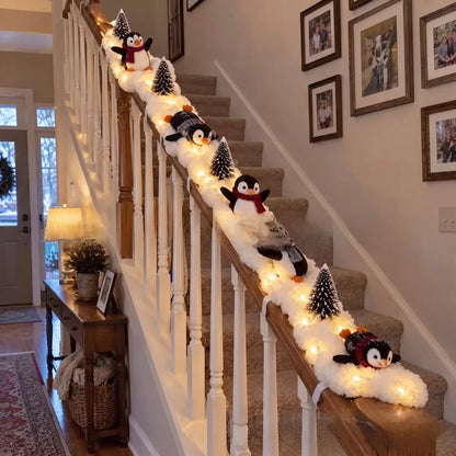 Penguin Christmas decor sliding down a staircase banister with snow garland, trees and fairy lights